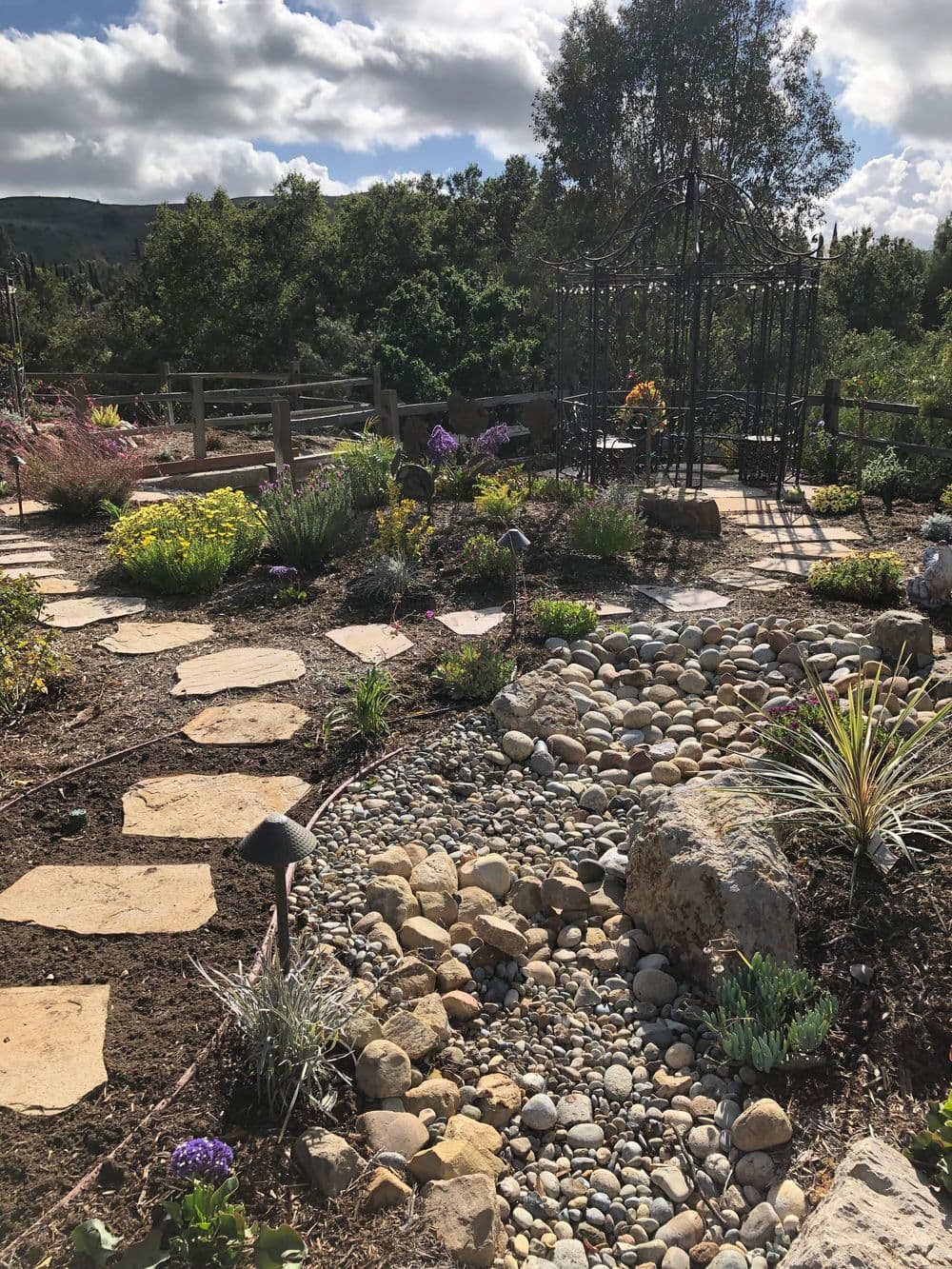 Beautiful garden pathway with rocks, flowers, and decorative gazebo under a cloudy sky.